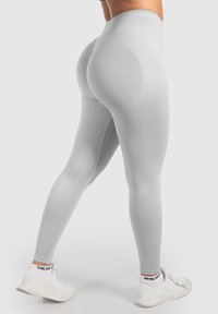 Leggings taille haute, gris clair, en tissu extensible, avec une texture douce et une coupe ajustée, assortis à des baskets blanches.