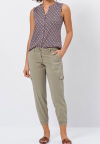 Blouse sans manches à motifs avec un col en V, associé à un pantalon cargo vert clair avec des poches lat érales et des poignets élastiques, complété par des sandales marron.