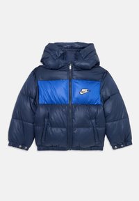 Námornícka puffer bunda s modrou hrudnou panelou, kapucňou a zipsom. Obsahuje elastické manžety a detail loga na ľavej strane. Hladká textúra.
