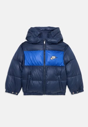 Doudoune navy avec panneau décolleté bleu, capuche et fermeture éclair. Écope des poignets élastiques et détail de logo sur le côté gauche. Texture lisse.