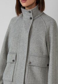 Grau gemusterter Fischgrätenmantel mit hohem Kragen, Druckknöpfen und zwei Fronttaschen. Der Stoff hat eine weiche Textur, die Wärme und Schutz bietet.