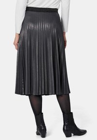 Grijze plissé rok met een glanzende afwerking, voorzien van een zwarte elastische tailleband en gecombineerd met zwarte enkellaarsjes.