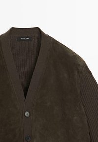 Cardigan marrone con colletto in maglia testurizzata e corpo in suede. Presenta un collo a V, chiusura a bottoni e due dettagli con bottoni frontalmente.