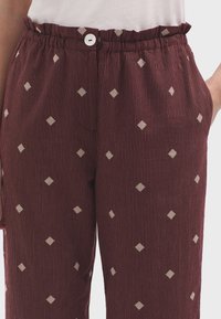 Pantalons rayés bordeaux avec une taille froncée, fermeture à bouton blanc et motifs en diamant brodés. Comprend des poches latérales.