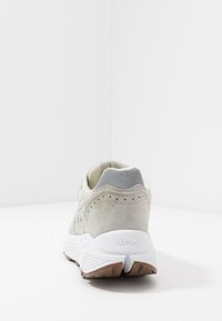 Lys grå sneaker i suede materiale, polstret krave og hvid mellemsål. Gummiydersål med et tekstureret mønster for greb.