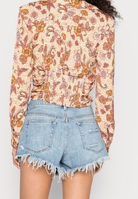 Blusa con stampa floreale e schiena arricciata, caratterizzata da maniche lunghe; abbinata a pantaloni corti in denim leggero blu con orlo sfilacciato.