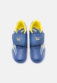Ζευγάρι παιδικά παπούτσια ποδοσφαίρου μπλε και κίτρινα με λουράκια Velcro, υφή στην επιφάνεια και λογότυπο "Joma" σε λευκό φόντο.