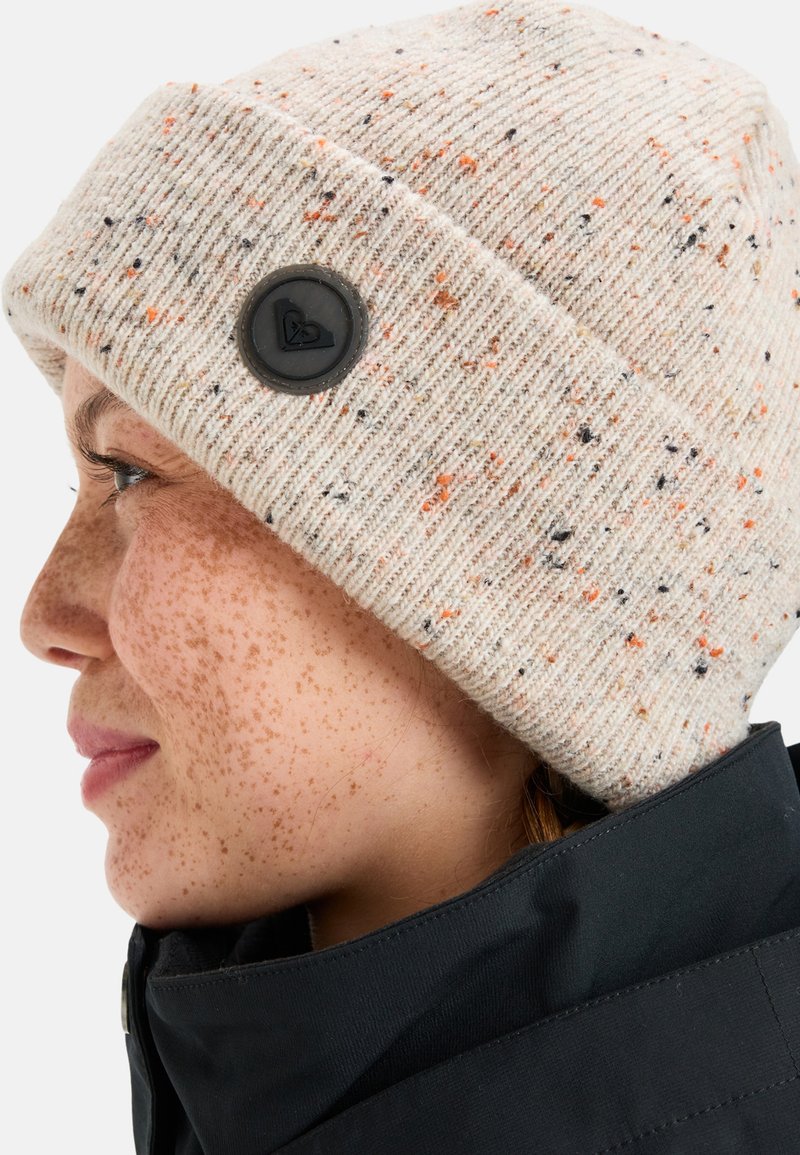 Beige Strickmütze mit orangefarbenen und schwarzen Sprenkeln, mit einem schwarzen Logo-Button. Gerippte Textur, umgeschlagenes Bündchen-Design.