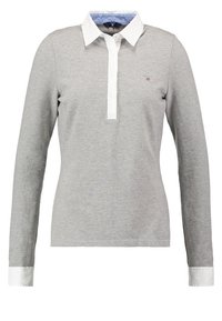 Camisa polo de manga larga gris, fabricada con un tejido suave, con un color blanco en el cuello y una botonadura, que presenta un detalle interior en azul en el cuello.