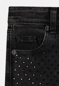 Jeans de mezclilla negra con un diseño ajustado, detalles de ojales multicolores en toda la tela y un pequeño bolsillo frontal.