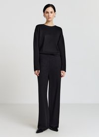 Maglione nero in maglia con scollo rotondo, abbinato a pantaloni neri a vita alta e gambe larghe. Tessuto liscio e vestibilità comoda. Scarpe nere.