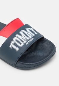 Infradito blu navy con cinturino in sintetico liscio caratterizzato da dettagli rossi e bianchi e il logo "TOMMY HILFIGER" in bianco. Suola texturizzata.