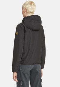 Giacca imbottita nera con cappuccio, dotata di chiusura con cerniera, polsini elasticizzati e distintivo sulla spalla sinistra, abbinata a pantaloni cargo grigi.