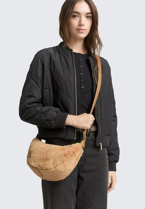 Giacca bomber nera trapuntata con polsini a costine, abbinata a una borsa a tracolla in pelliccia sintetica beige con spallina. Jeans scuri completano l'outfit.