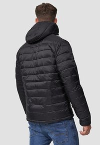 Veste matelassée noire avec des coutures horizontales, une capuche et des poignets élastiques. Fabriquée en matériau brillant et résistant à l'eau.