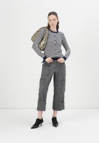 Cardigan cu dungi bleumarin și alb, pantaloni cargo gri cu buzunare, pantofi cu toc negri cu șireturi și o geantă supradimensionată cu model.