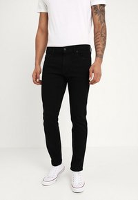 Svarta slim-fit jeans med femficksdesign, enfärgad, och klassisk knappstängning. Bärs med en vit T-shirt och vita sneakers.