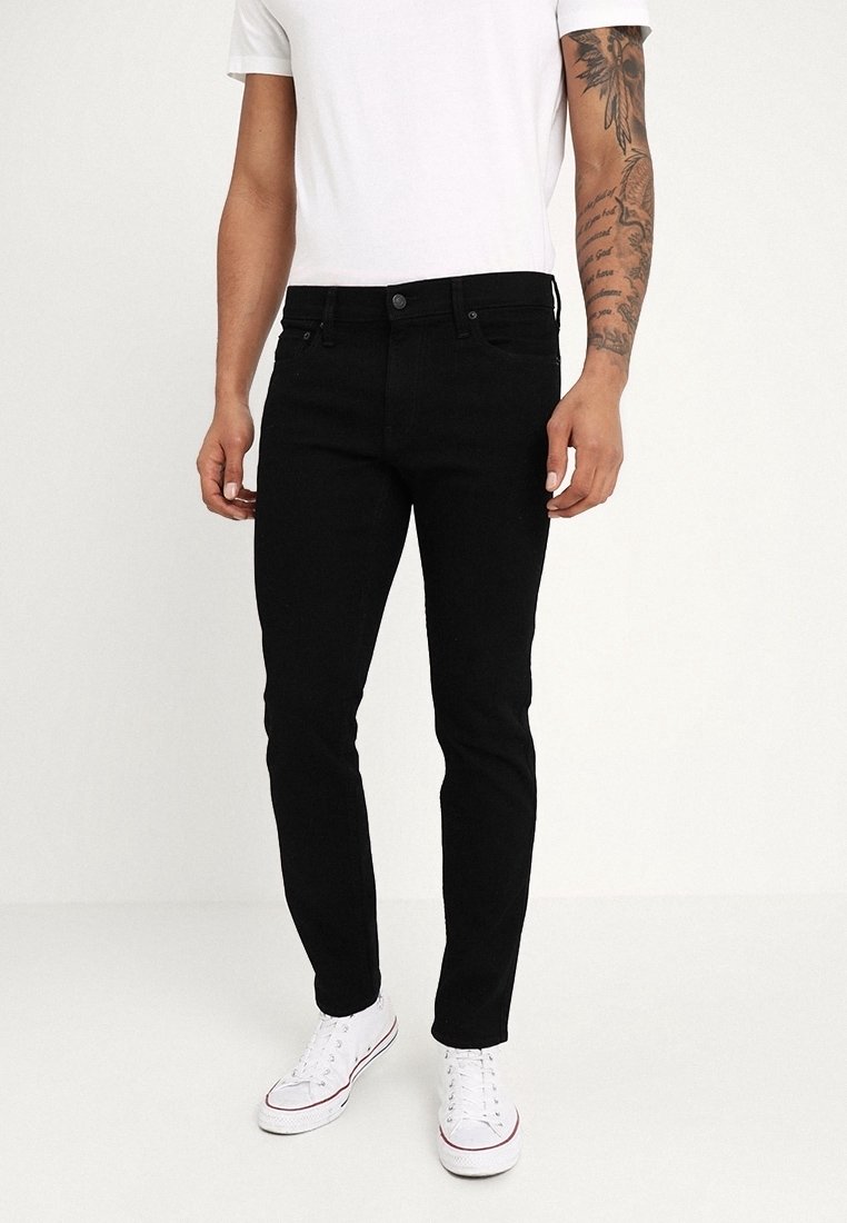Svarta slim-fit jeans med femficksdesign, enfärgad, och klassisk knappstängning. Bärs med en vit T-shirt och vita sneakers.