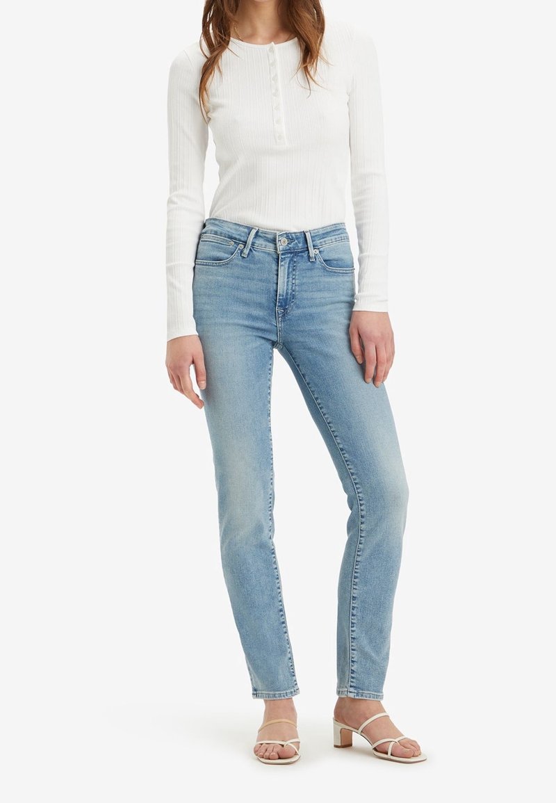 Svetle modré džíny s rovnými nohavicemi, vysokým pasem a minimálním vyblednutím, spárované s bílým vrškem s dlouhým rukávem a sandály na pásky.