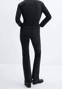 Jeans de denim negro con un corte recto, detalles sutiles en los bolsillos traseros y acentos de costura. Combinados con botas negras hasta el tobillo.
