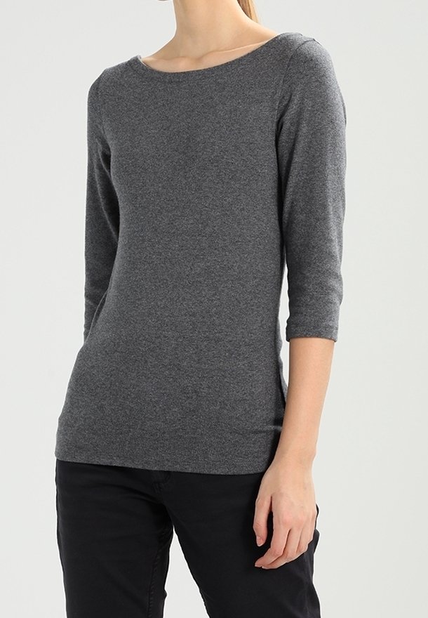 Graues Oberteil mit dreiviertelärmeln aus weichem Strickstoff, mit einem Schiffsdekolleté und einer figurnahen Silhouette, kombiniert mit schwarzen Hosen.