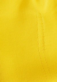 Gros plan sur un tissu côtelé jaune avec une couture verticale détaillée sur le côté droit.