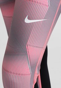 Leggings de Nike con un patrón de rayas grises y rosas, textura suave y un logo blanco en el lateral. Vista en primer plano del diseño.