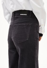 Svarta kordbyxor med hög midja, med två bakfickor och en platt midja med en logotagg. Strukturerad tyg med vertikala ribbor.