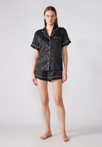 Ensemble de pyjama en satin noir avec un imprimé léopard, manches courtes et piping blanc, comprenant un haut à col et un short assorti.