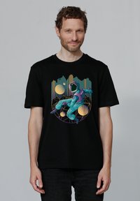 Schwarzes T-Shirt mit einem Grafikdesign eines Astronauten in Türkis, mit lila Akzenten, umgeben von bunten geometrischen Formen und Kreisen.