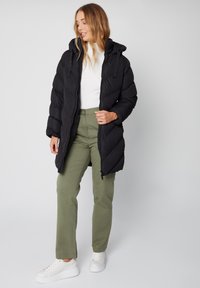 Abrigo negro acolchado con capucha, con diseño acolchonado y cierre de cremallera. Combinado con pantalones verde oliva y zapatillas blancas.