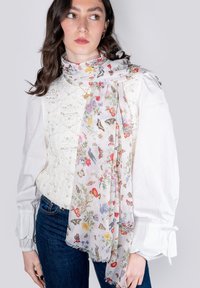 Sciarpa floreale leggera con sfondo bianco decorata da fiori colorati e farfalle, rifinita con bordi frangiati.
