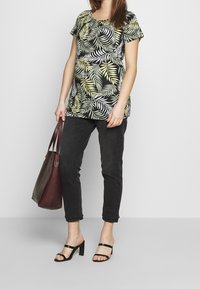 Černá květinová tunika s vzory zelených a žlutých listů, spárovaná s černými džíny a černými sandály na blokovém podpatku. Zahrnuta je také vínová taška.