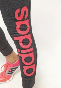 Bentröja med stort rött "adidas"-tryck på mörkgrått tyg och en fot iklädd en rosa och grå sportskor.