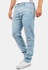 Lichtblauwe gestreepte jeans met een slim fit, voorzien van een knoopsluiting en voorzakken. Gecombineerd met witte sneakers met rode accenten.