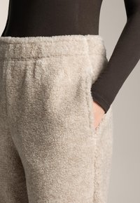 Kremno obarvane hlače iz flisa z mehko, teksturirano površino. Imajo stranske žepke in elastični pas, zasnovane za udobje in toplino.