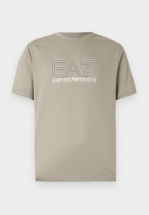 Béžové tričko s krátkým rukávem s logem "EA7 Emporio Armani" v bílé barvě s černým obrysem na hrudi, zobrazené na neutrálním pozadí.