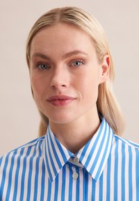 Camicia a righe blu e bianche con colletto classico, chiusura a bottoni e una texture di tessuto liscia. Le righe sono uniformemente distanziate e nitide.