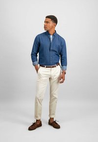 Denim marškiniai su mygtukais, su rūkytais rankovėmis, bežiniai chinos kelnes ir rudos odinės valtinės bateliai. Minimalistinis dizainas, pritaikytas fasonas ir jokios matomos raštų.