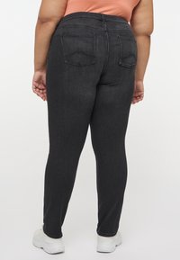 Mörka skinny jeans i denim med hög midja, med bakfickor och en slät, texturerad finish. Matchas med vita sneakers.