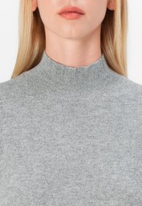 Sivkasta pletena pulover s visokim rebrastim ovratnikom, ki ima mehak teksturo in prilegajoč dizajn. Tkanina se zdi lahka in gladka.