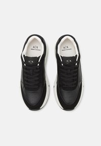 Baskets de sport noires avec des tiges en cuir lisse et en tissu. Les caractéristiques comprennent un bout rond, des lacets plats et une semelle en caoutchouc blanche avec des accents subtils.