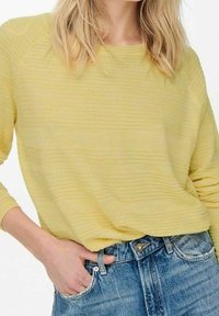 Helles, strukturiertes gelbes Sweatshirt mit bequemer Passform, mit rundem Halsausschnitt und langen Ärmeln. Kombiniert mit klassischen blauen Jeans.