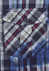 Marinblaues und karierte Hemd mit Knöpfen, das eine Tasche mit "JV"-Stickerei, einen schwarzen Knopf und einen strukturierten Stoff mit sich kreuzenden roten und grünen Linien aufweist.