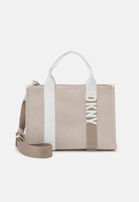 Sac à main en toile beige avec des accents en cuir blanc, des poignées supérieures et une bandoulière amovible. Présente un logo DKNY bien en vue sur le côté.
