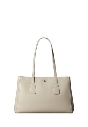 Beige lædertaske med to lange håndtag og lille sølv "cK" logo centreret nær den øverste kant.