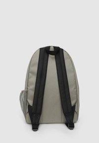 Zaino in tessuto grigio con spallacci neri regolabili e maniglia superiore. Presenta tasche laterali in rete per riporre oggetti. Texture liscia, forma arrotondata.