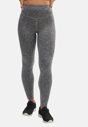 Leggings grises con un patrón texturizado, cinturilla alta y diseño ajustado. Combinados con zapatillas deportivas negras.