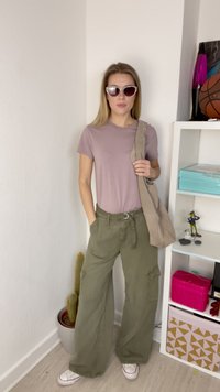 Lyslilla t-shirt, olivengrøn brede cargobukser med lommer, beige skuldertaske og hvide sneaker; oversized solbriller fuldender looket.