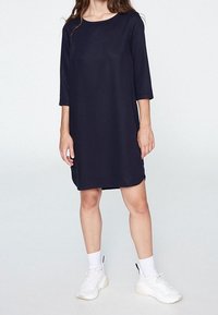 Mörkblå shiftklänning med trekvartsärmar, tillverkad av slätt tyg, kombinerad med vita sneakers och ankellång strumpor.